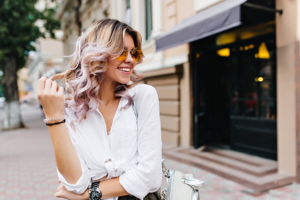 Happy young blonde woman touching her hair which is dip-dyed in pink